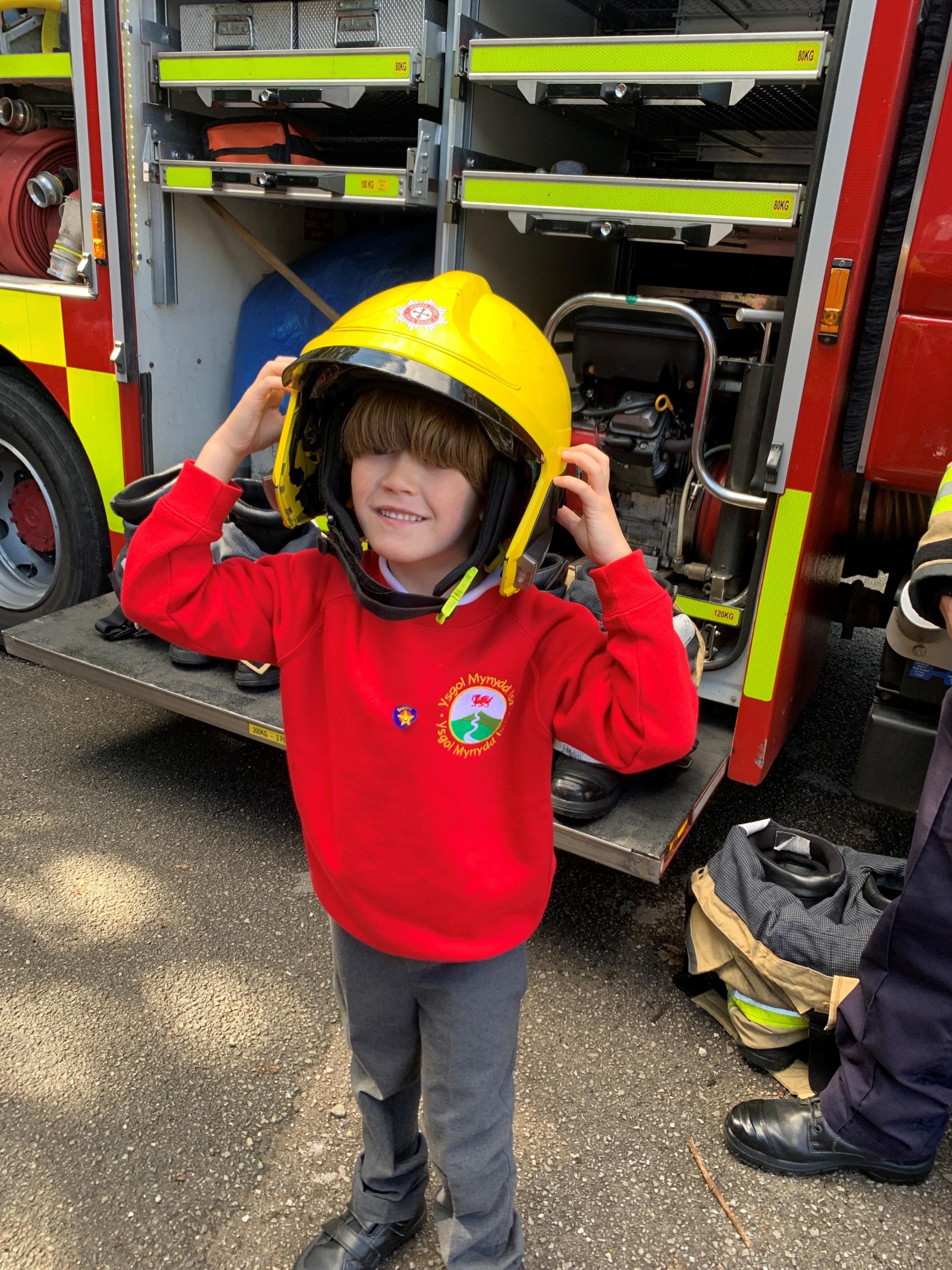 Trying on a firefighters helmet at Ysgol Mynydd Isa.