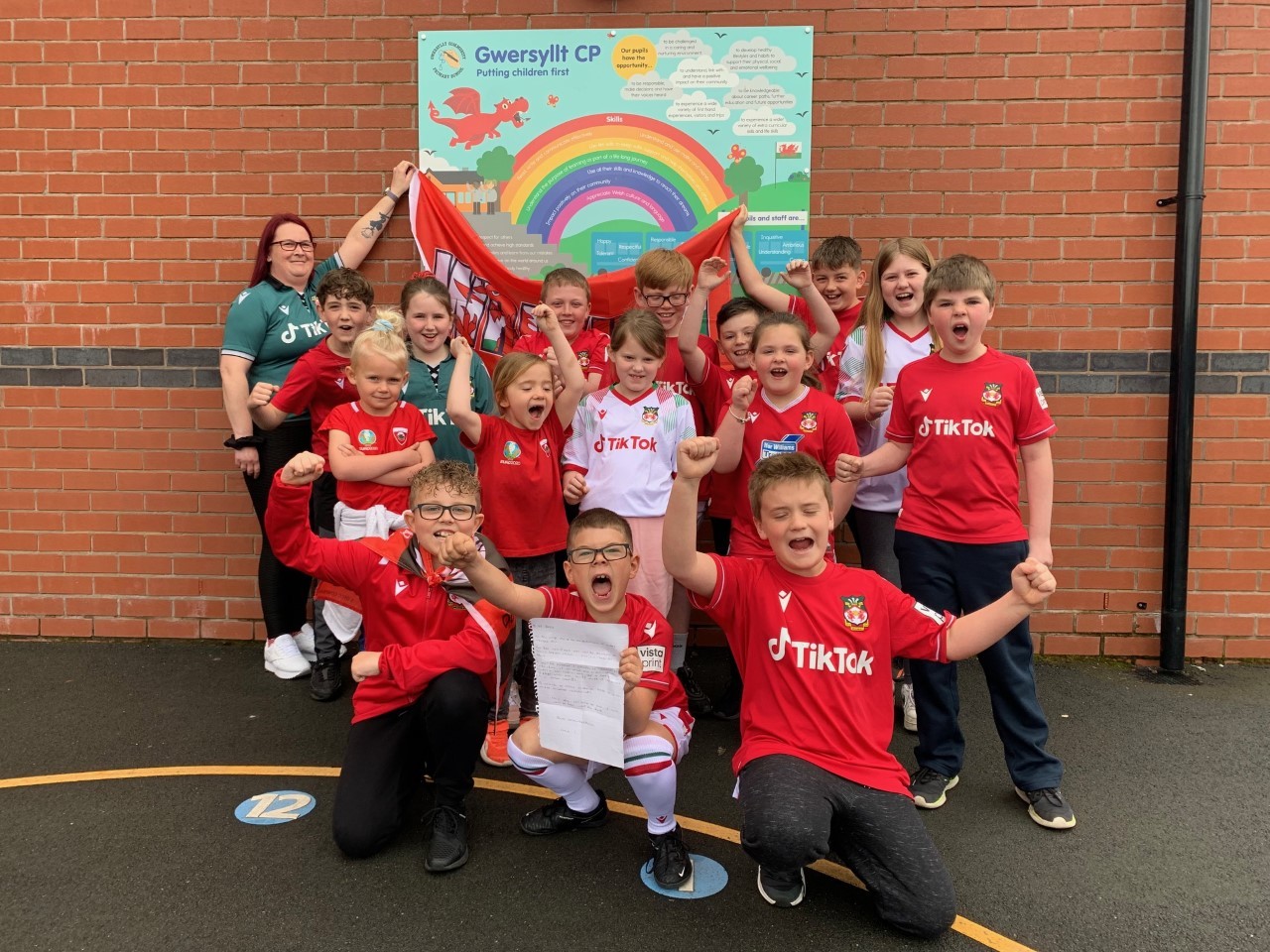 Oscar Hernandez Garcia (holding his letter) celebrating Wrexham AFCs promotion win, with staff and pupils at Gwersyllt CP School.