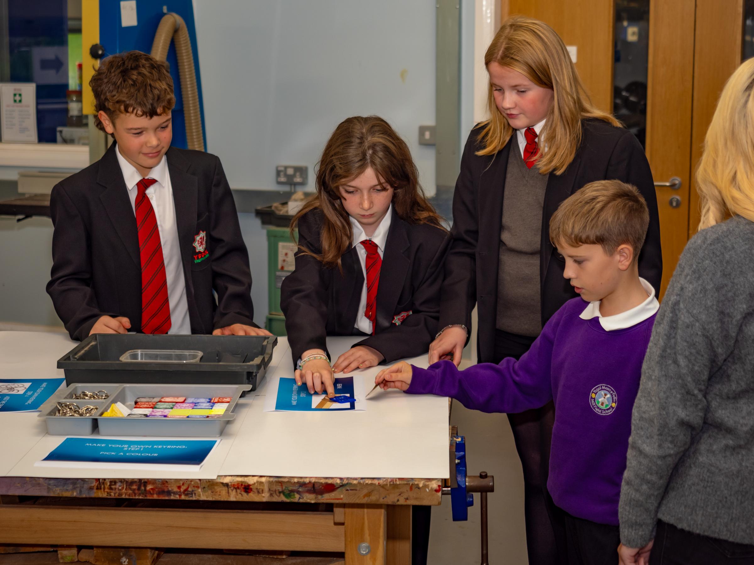 Ysgol Treffynnon students help visitors in design technology to make their own keyrings.